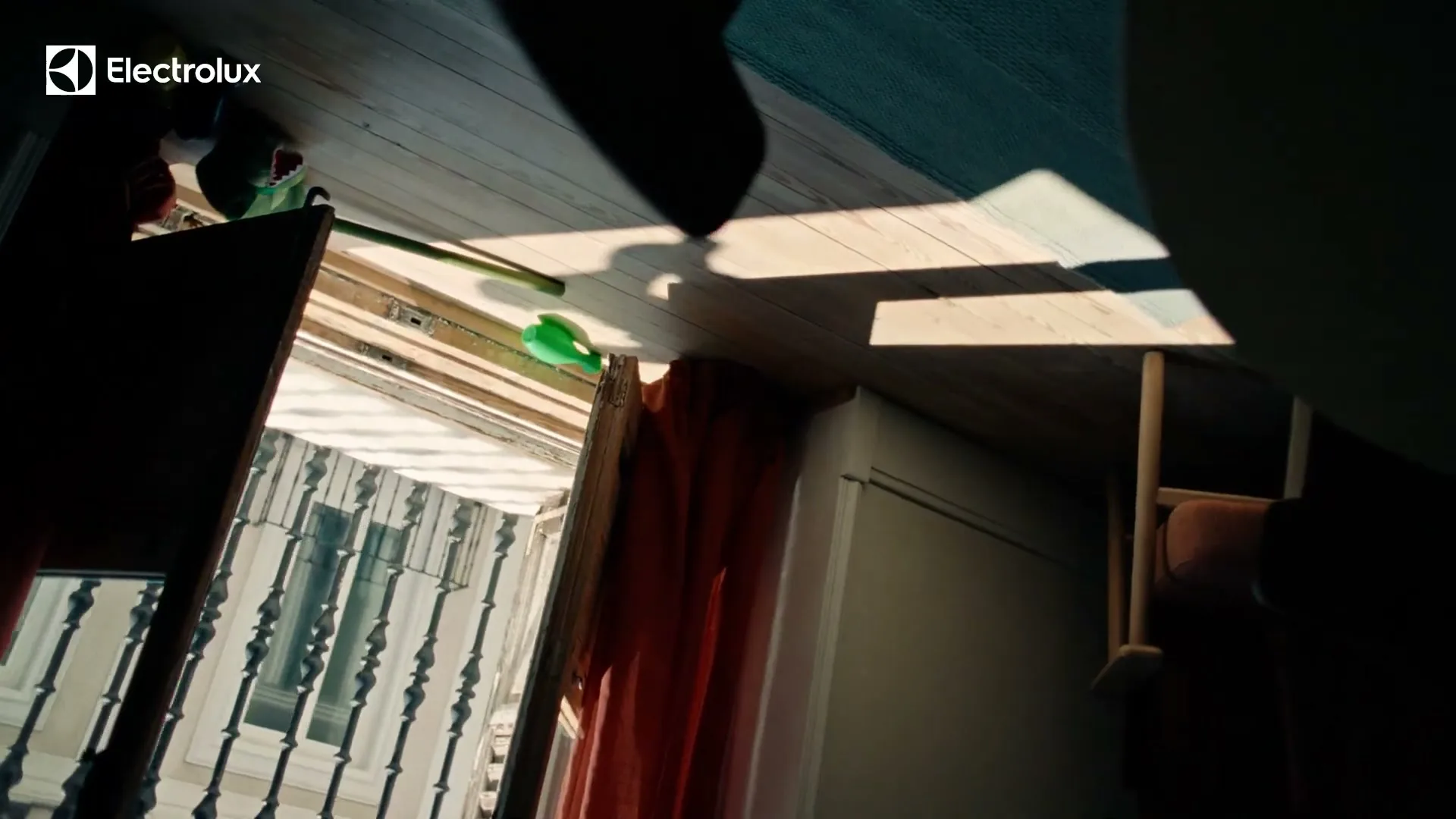 Sunlight streams through a window onto a wooden floor, revealing a broom and a red curtain in a domestic setting.