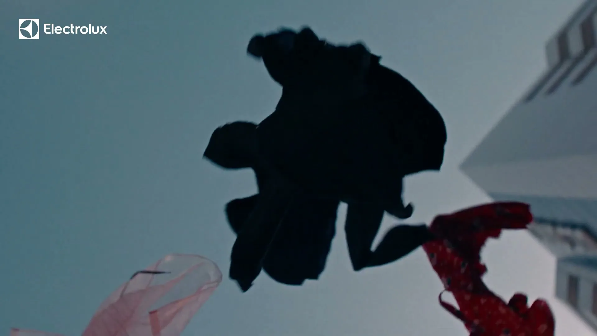 Silhouetted clothes, including a red floral dress, hang on a clothesline against a clear blue sky, swaying gently in the breeze.