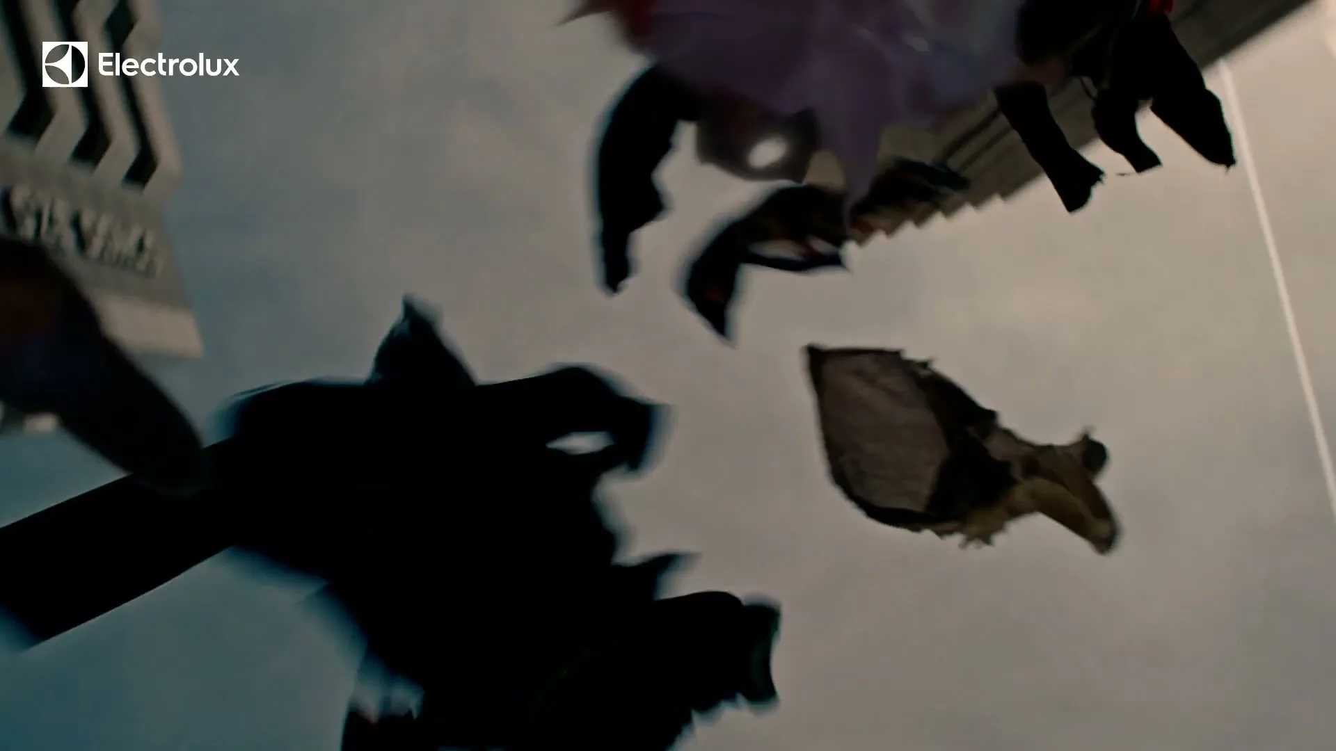 Clothes and other items fall from the sky, silhouetted against a cloudy blue sky, with tall buildings visible on the sides.