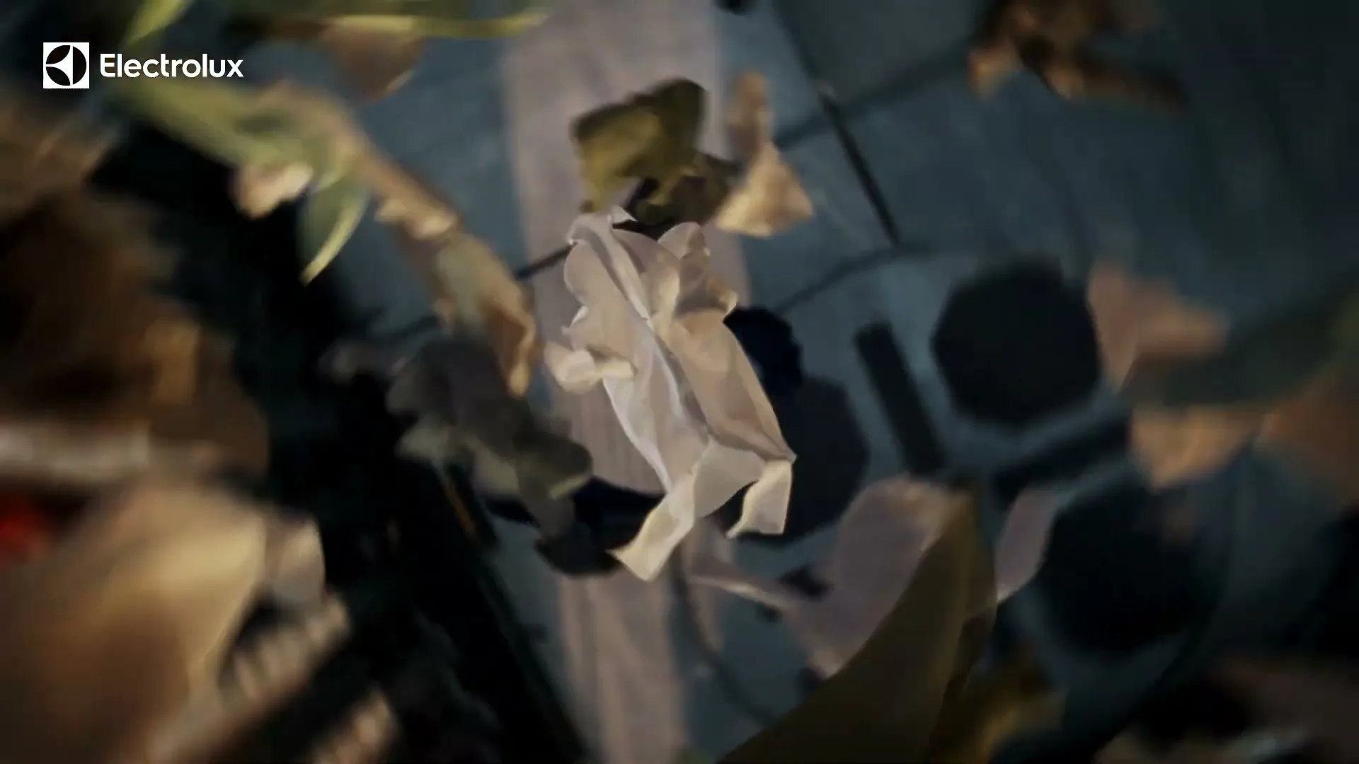 A white cloth and other fabric pieces are seen falling through the air, with a blurred background of a dark room.
