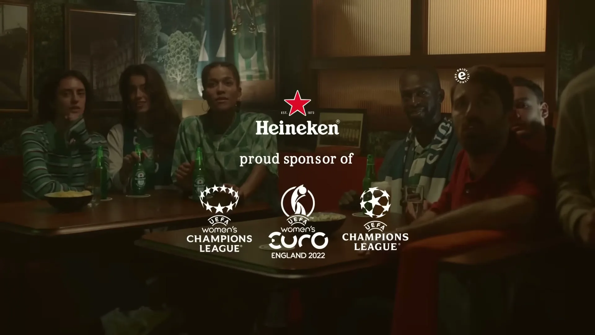 A group of diverse friends in a dimly lit bar watch a game, with Heineken bottles and logos appearing on screen.