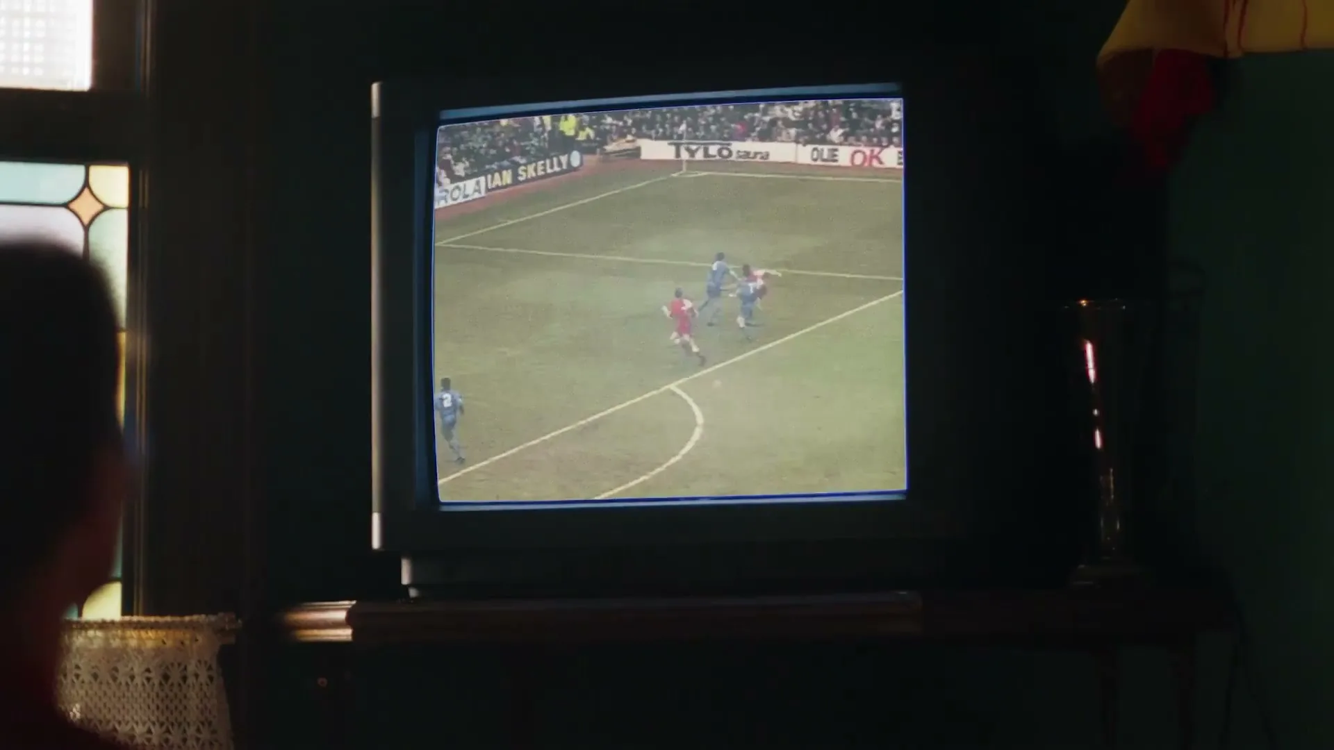 A person watches a vintage football match on an old television set, with the date "March 6, 1993" and the text "A hero of his time" appearing on screen.