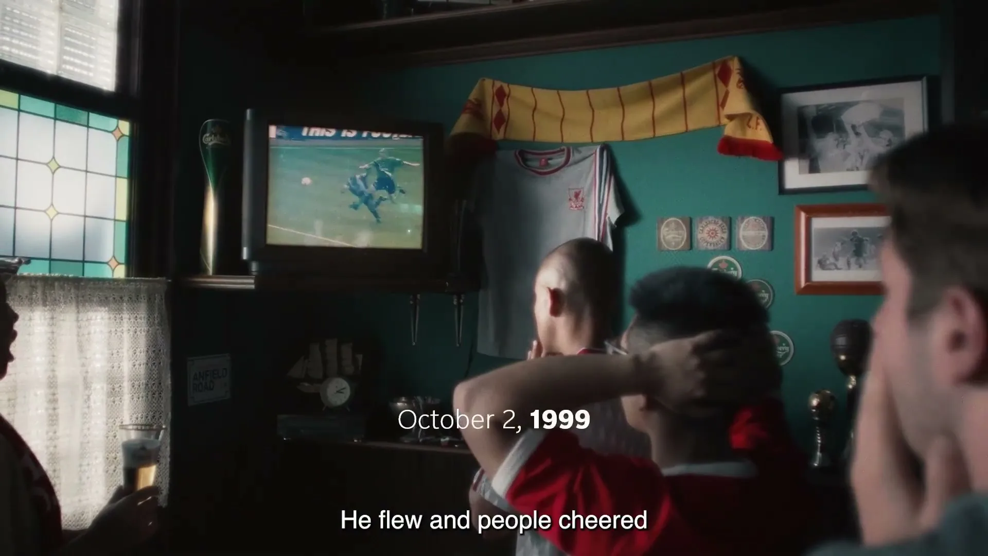 Three men in a pub watch a football match on an old TV, with one man holding his head in anticipation.