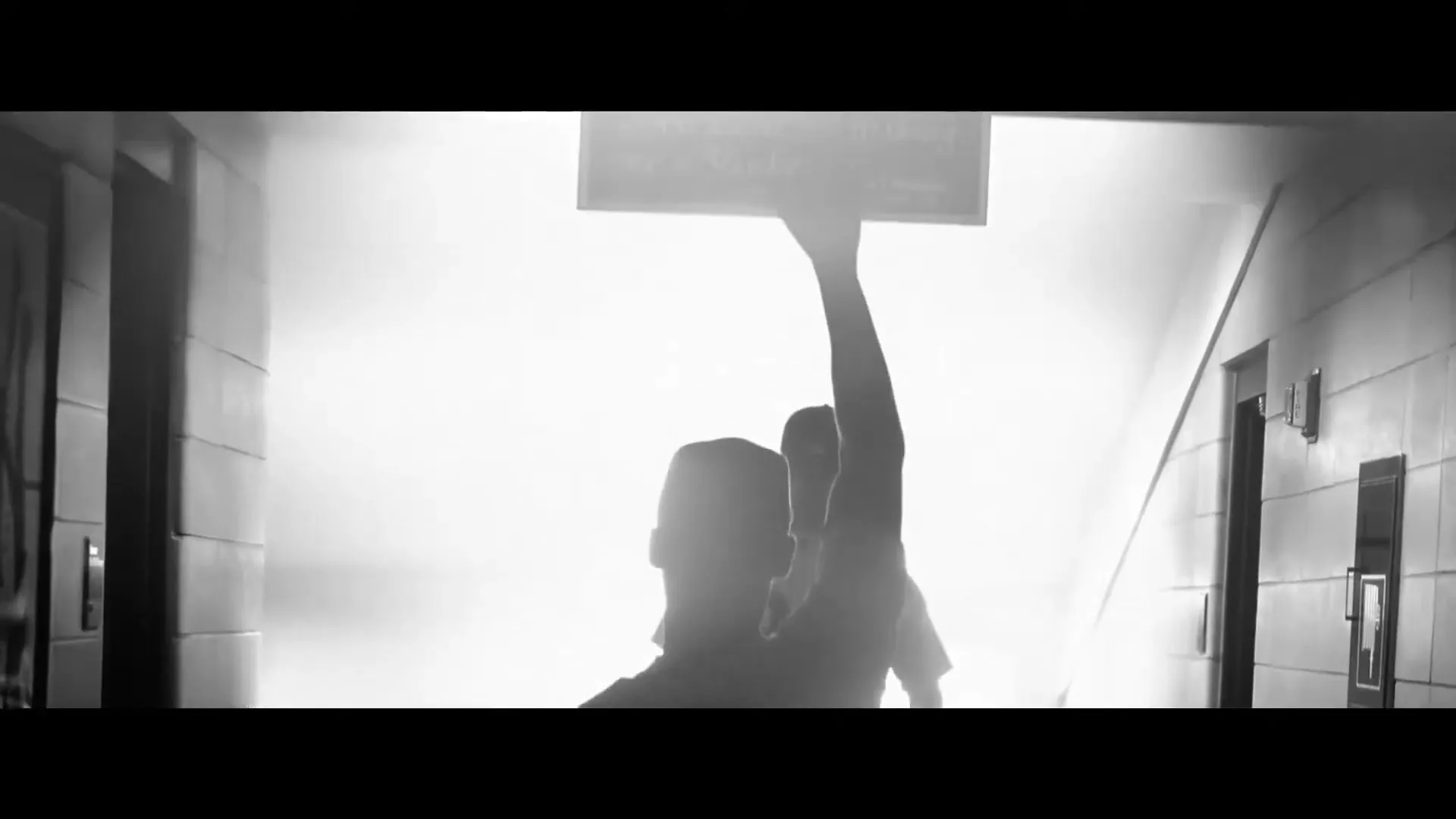 A silhouetted baseball player in a uniform reaches up to touch a sign hanging from the ceiling in a bright, hazy hallway.
