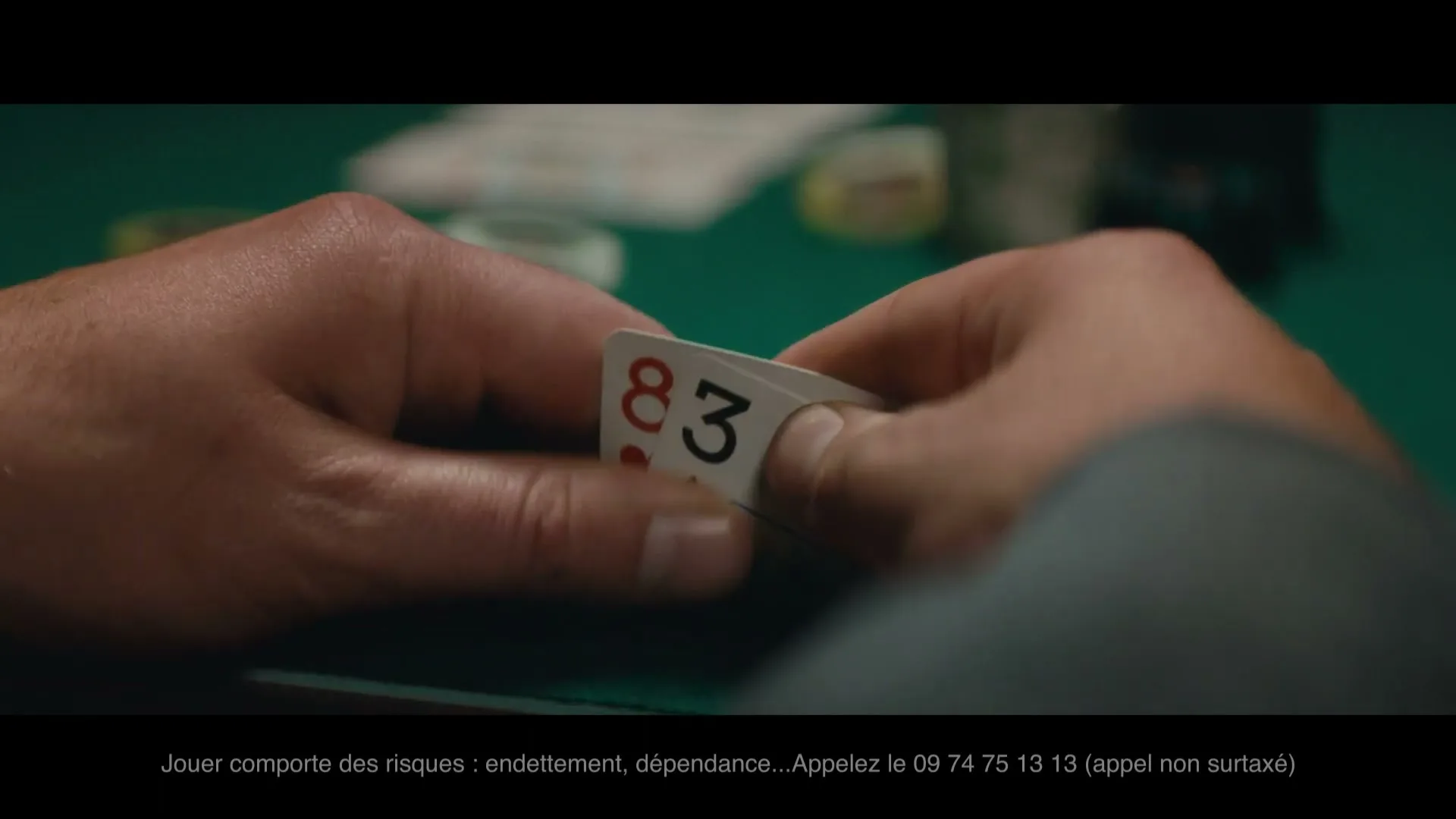 A man's hands are seen from a low angle, revealing his poker cards on a green felt table in a casino.