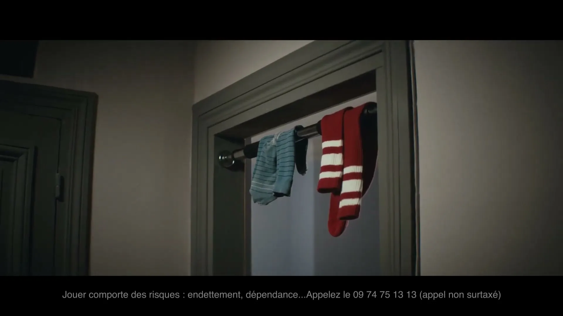 A pull-up bar is installed in a doorway, with a blue shirt and red and white striped socks hanging on it, in a dimly lit interior.
