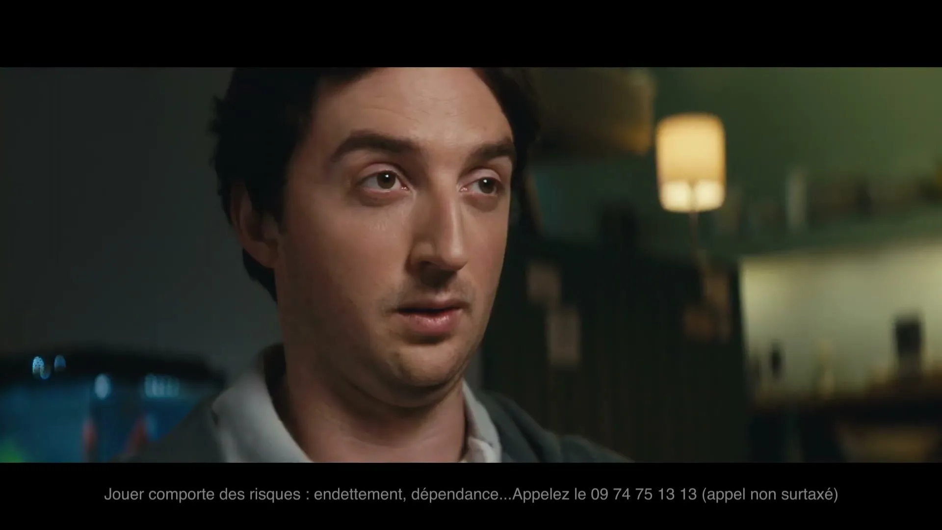 A man with dark hair and a grey hoodie looks forward with a slightly worried expression in a dimly lit interior.