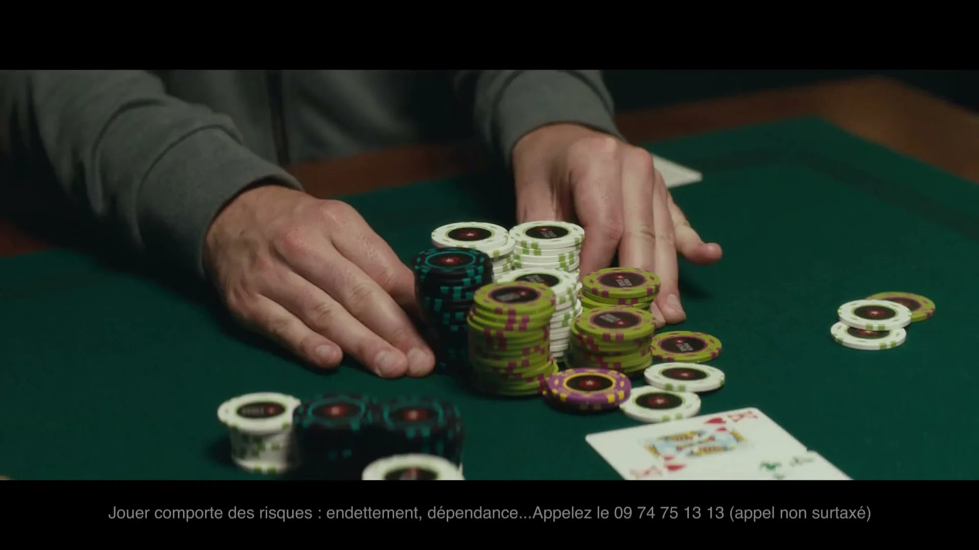A man's hands are shown on a green poker table, pushing a large stack of poker chips forward, with playing cards visible.
