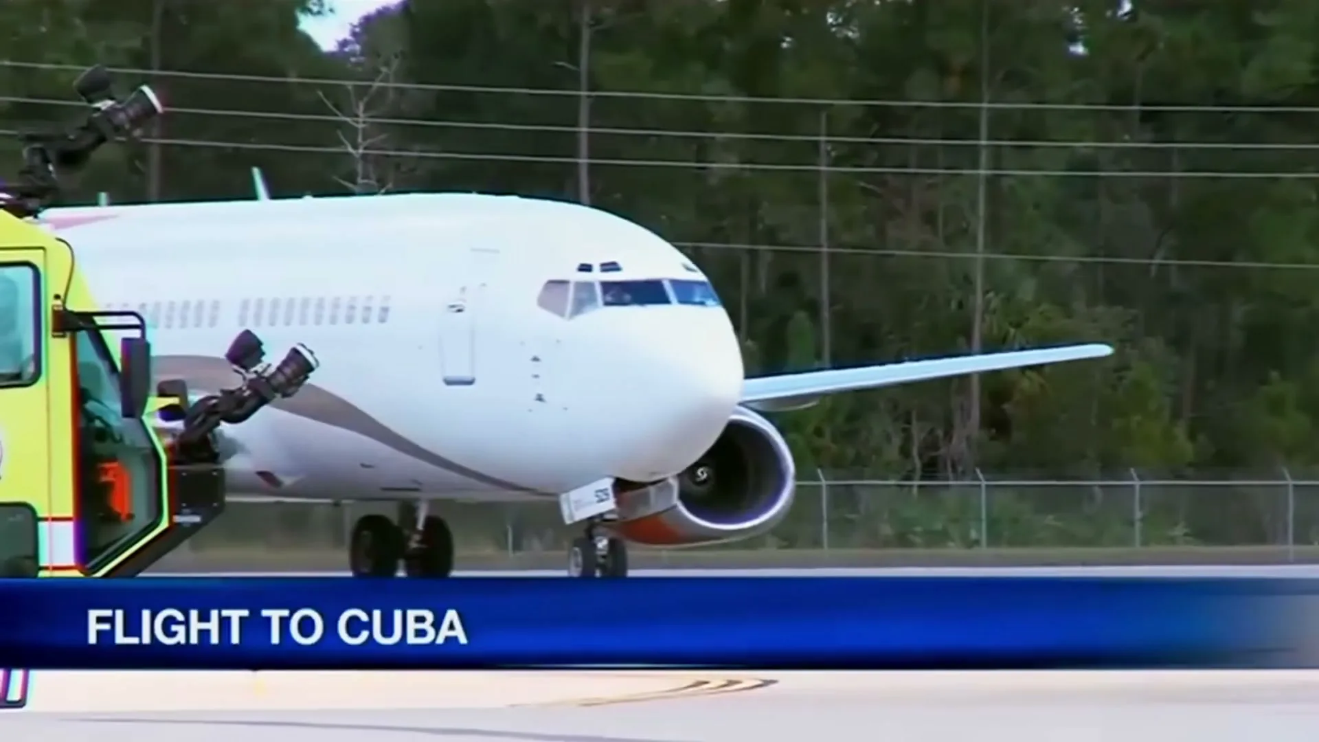A white airplane with orange tail is being towed on an airport tarmac, with a blue graphic overlay at the bottom.