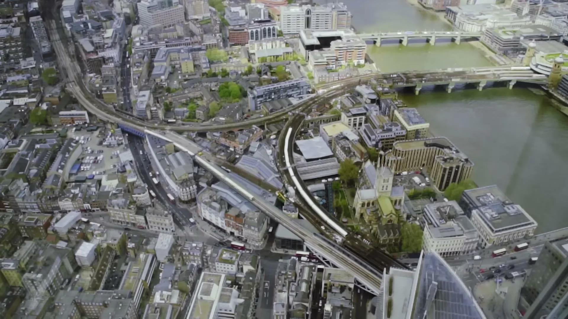 An aerial view of a bustling city with a river, bridges, and train tracks, showcasing urban infrastructure on a cloudy day.