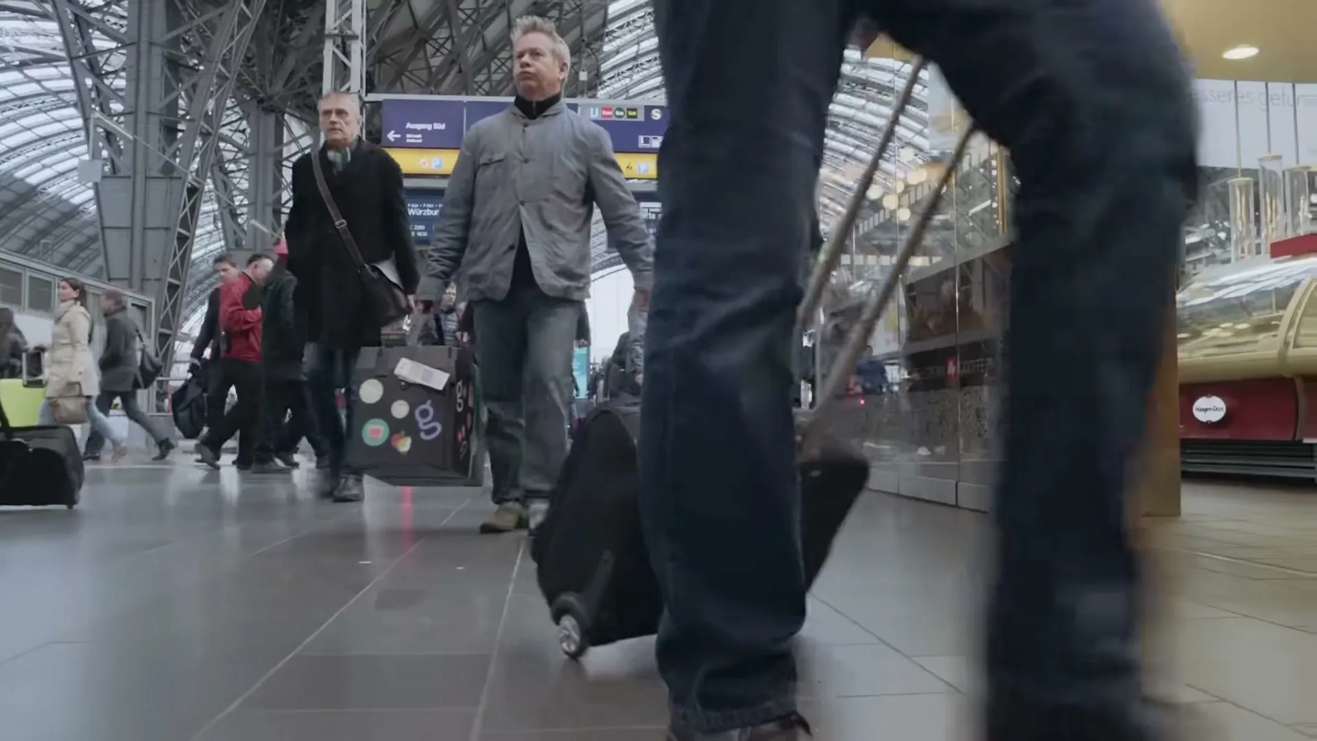 A low-angle shot of people walking through a busy train station, with a focus on the legs and luggage of a person in the foreground.