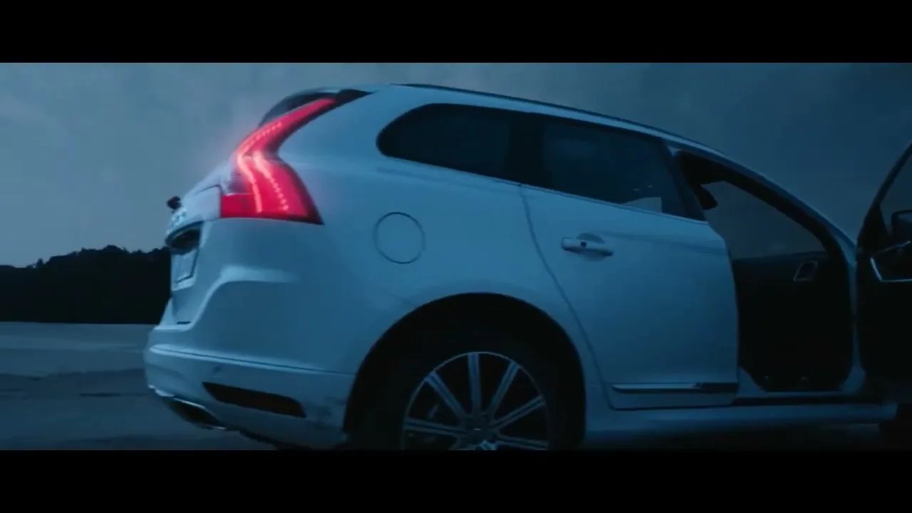 A white Volvo car is parked on a dark beach at dusk, with its door open and the ocean waves crashing in the background.