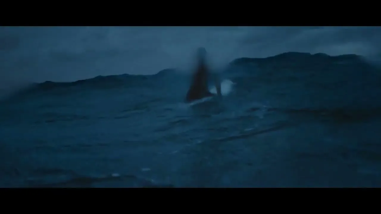 A female surfer in a wetsuit paddles through dark, choppy ocean waves under a stormy sky, looking up at the sky.