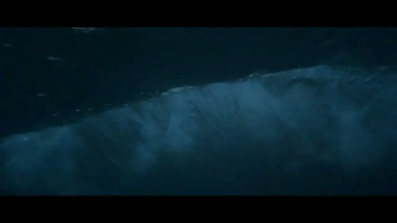 Underwater shot of a large wave breaking, showing the turbulent water and air bubbles, in a dark blue ocean.