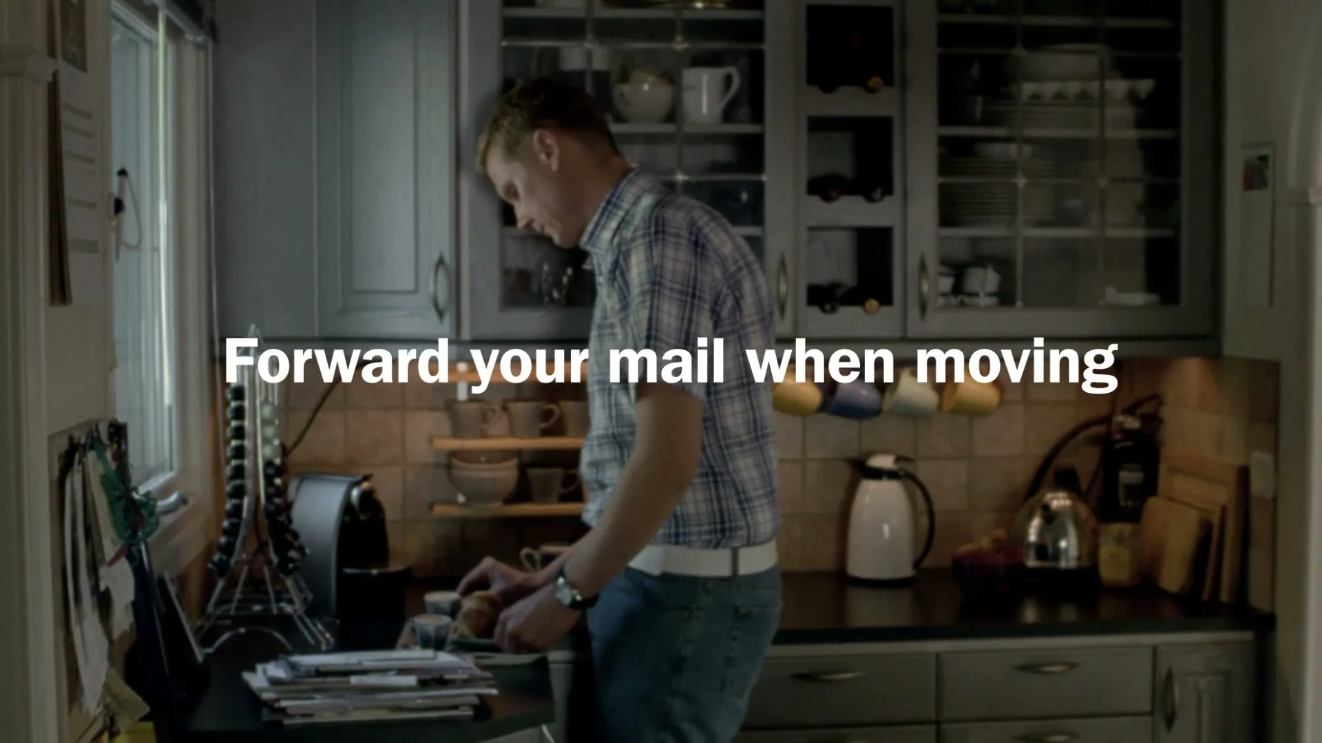 A man in his 30s wearing a plaid shirt and jeans is making coffee in a kitchen, with text overlayed on the screen.