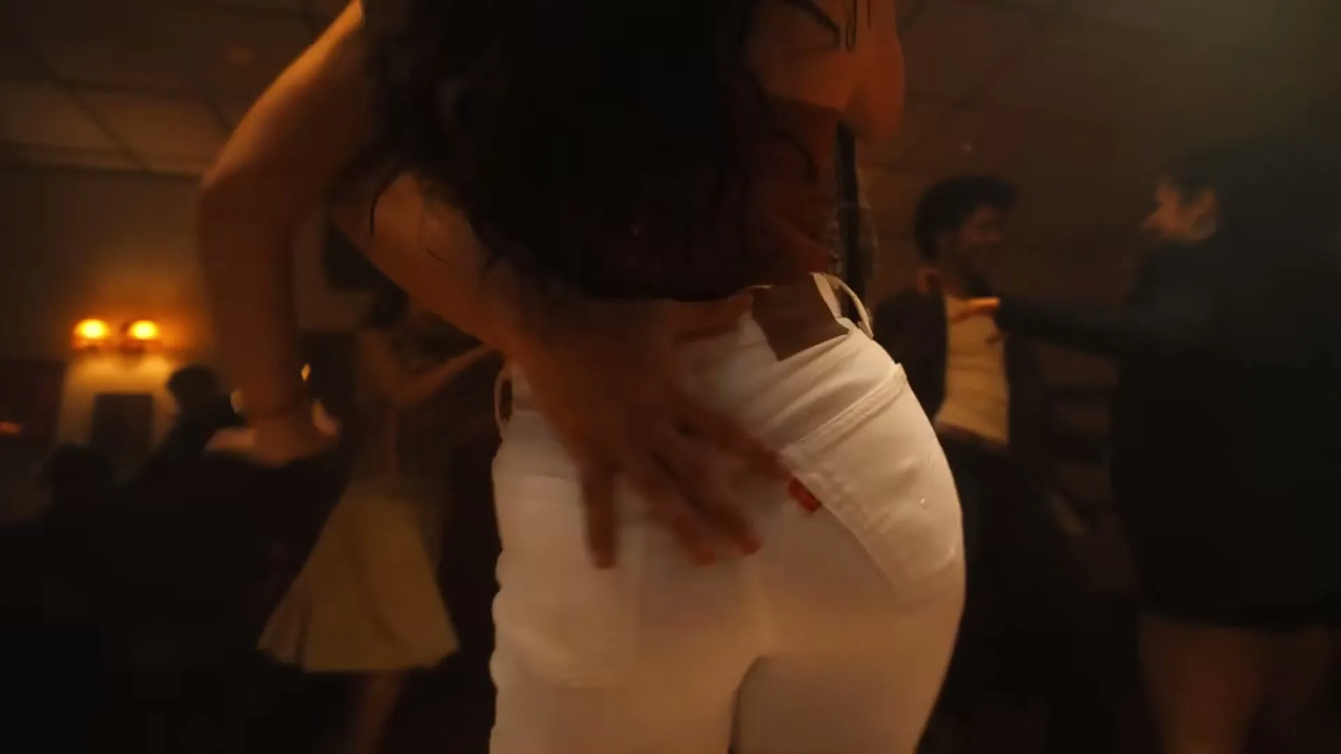 A woman in white Levi's jeans dances with a man, her hand on her hip, in a dimly lit club.