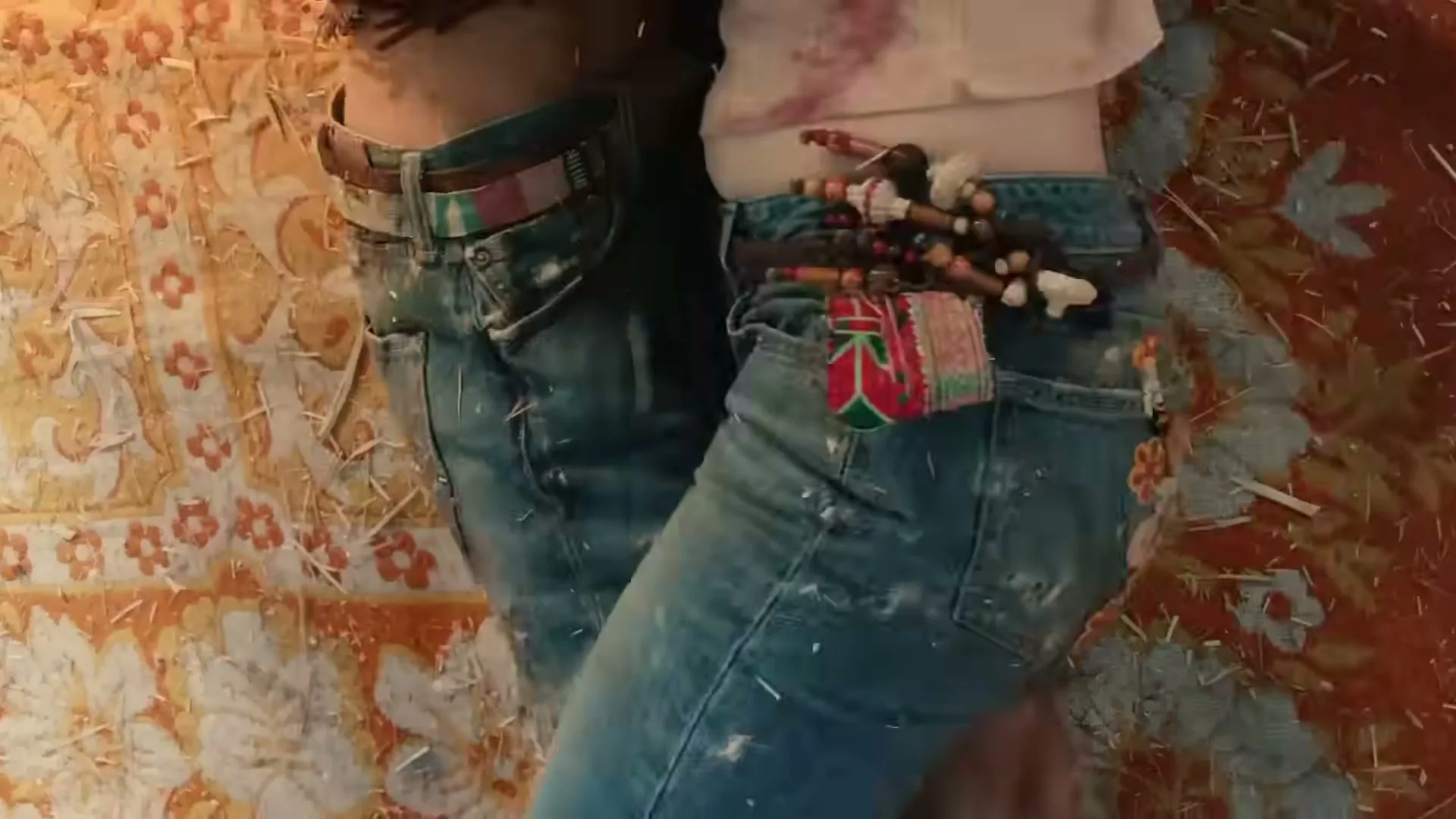 A person wearing custom painted Levi's jeans with floral designs is seen from behind, lying on a patterned rug with another person's arm around them.