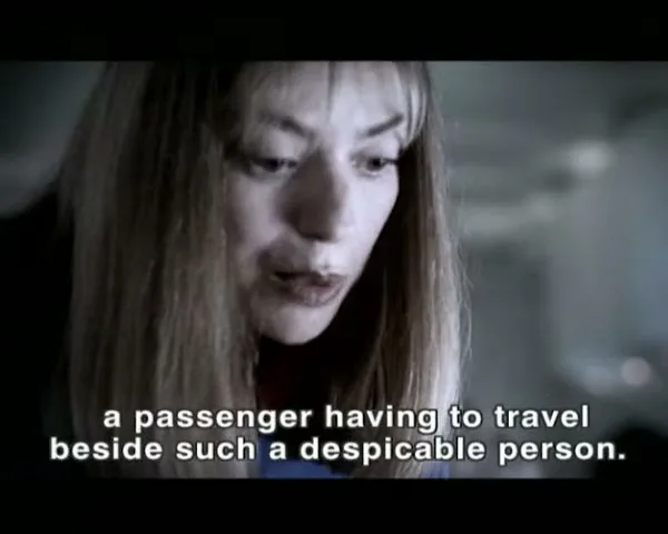 A woman with long blonde hair looks down and speaks, as a ghostly overlay of people on a bus appears, in an interior setting.