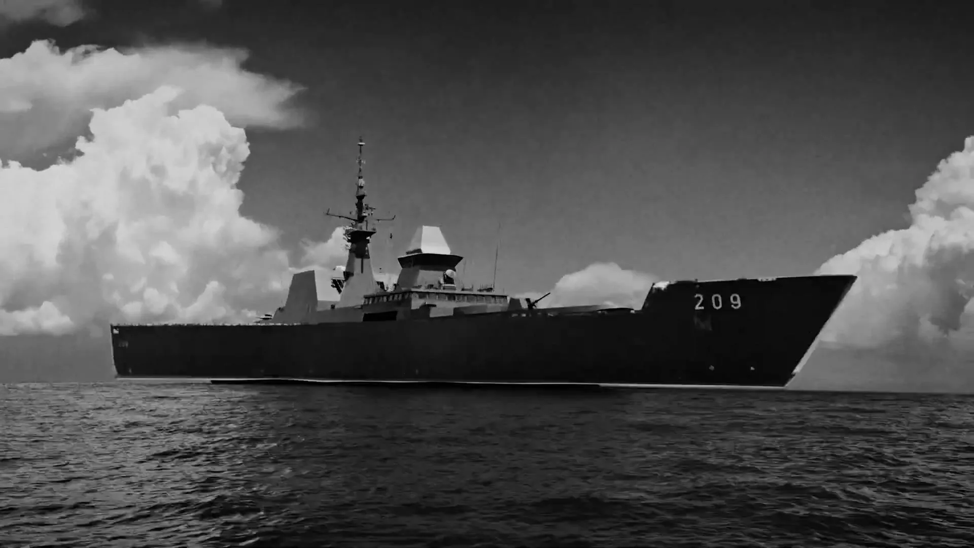 A black and white shot of a large naval warship sailing on the open ocean under a cloudy sky.