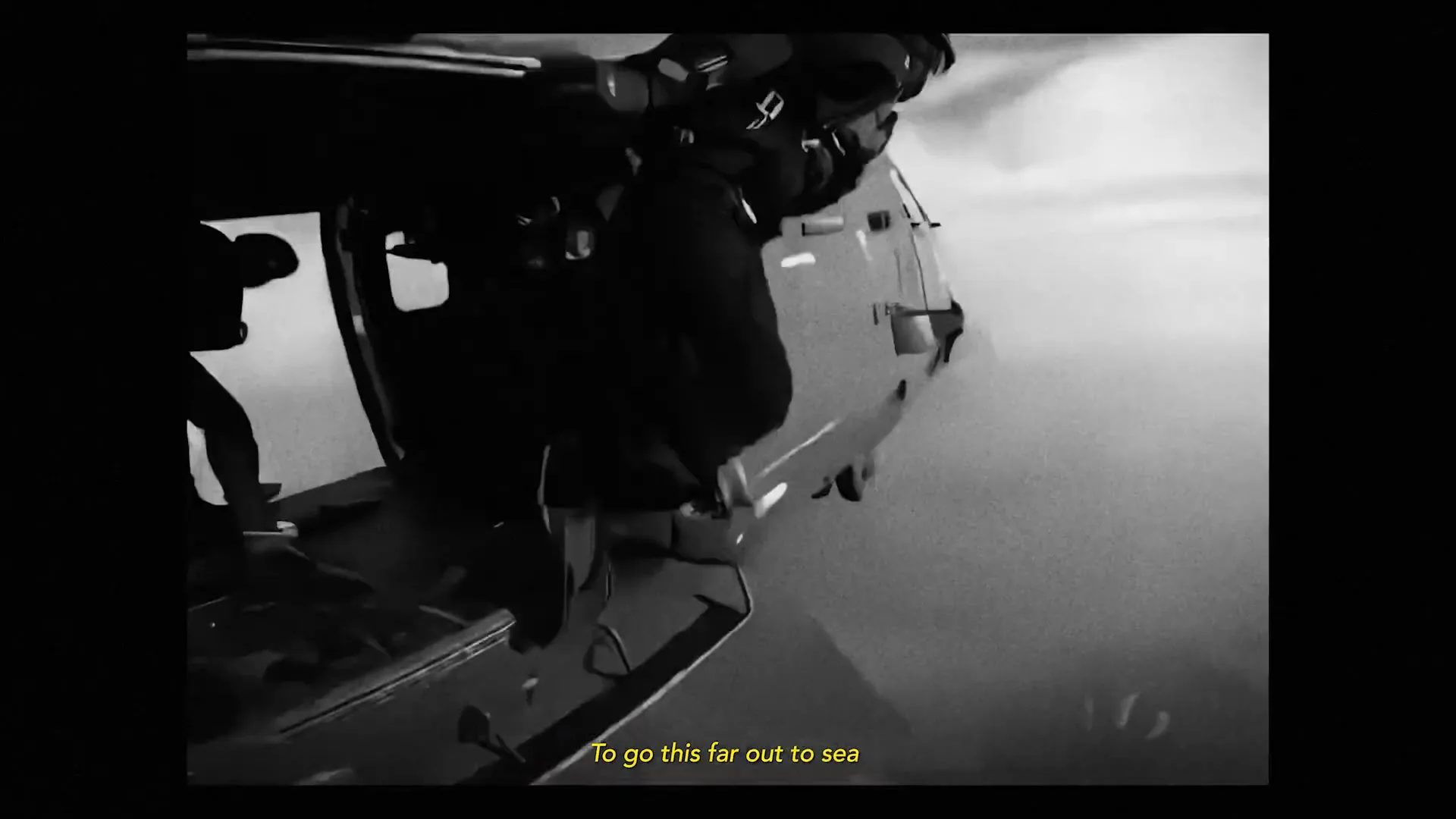 A person in military gear jumps out of a helicopter into the cloudy sky, captured in black and white.