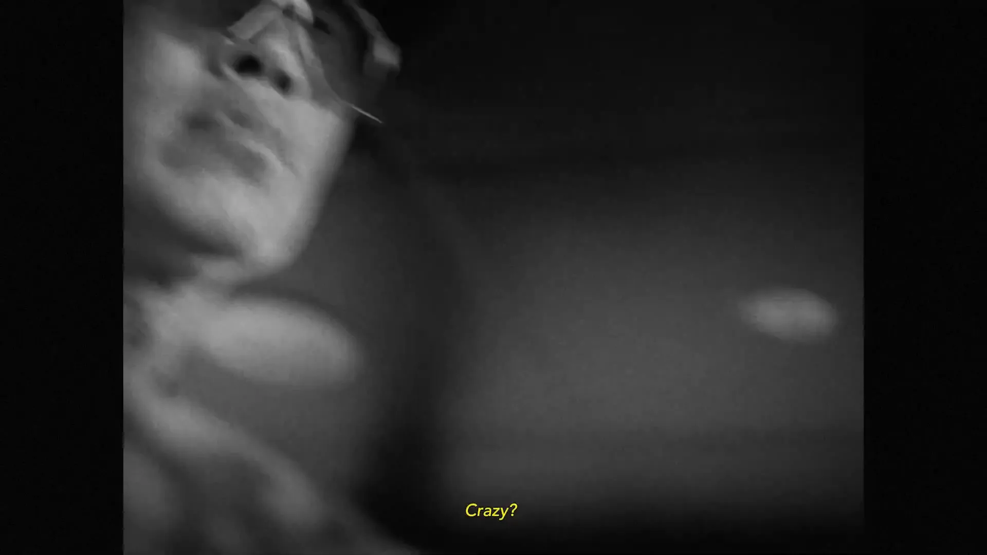 A man in a cap and goggles looks up, his face partially obscured by shadow, in a black and white, low-key shot.
