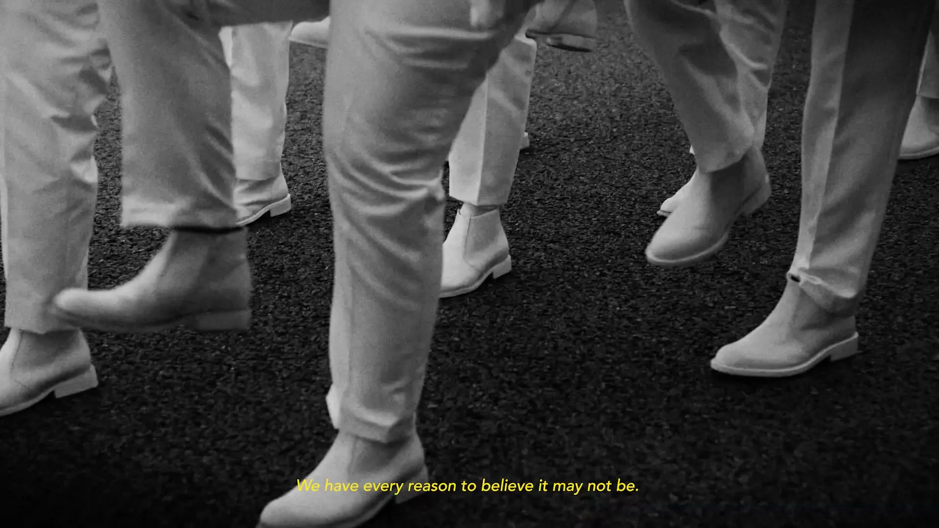 A group of young male naval officers in white uniforms march in formation outdoors under a cloudy sky, with yellow text overlayed.