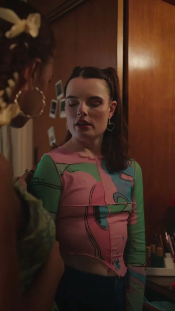 Two young women are in a bedroom, one looking distressed about her period while the other tries to comfort her, as they get ready to go out.