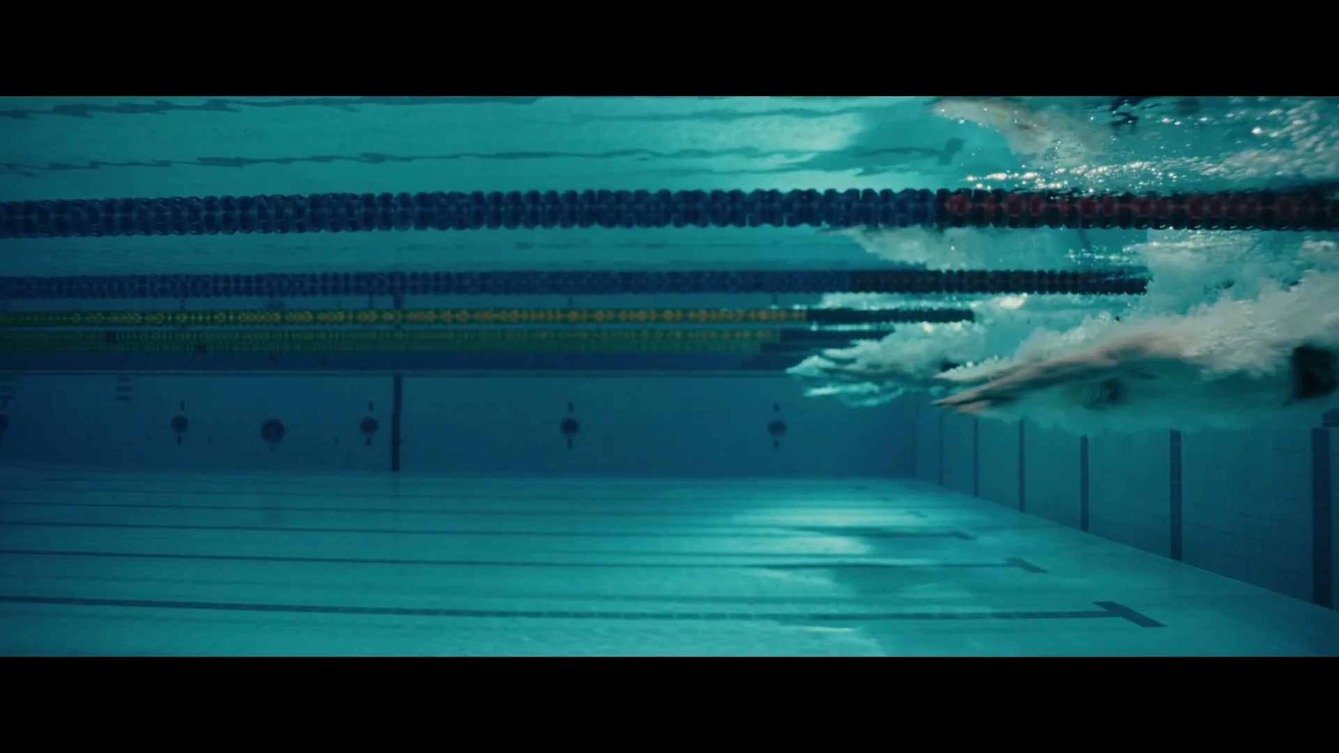 Underwater shot of a swimmer's arms and torso as they swim through a swimming pool, with lane ropes visible above.