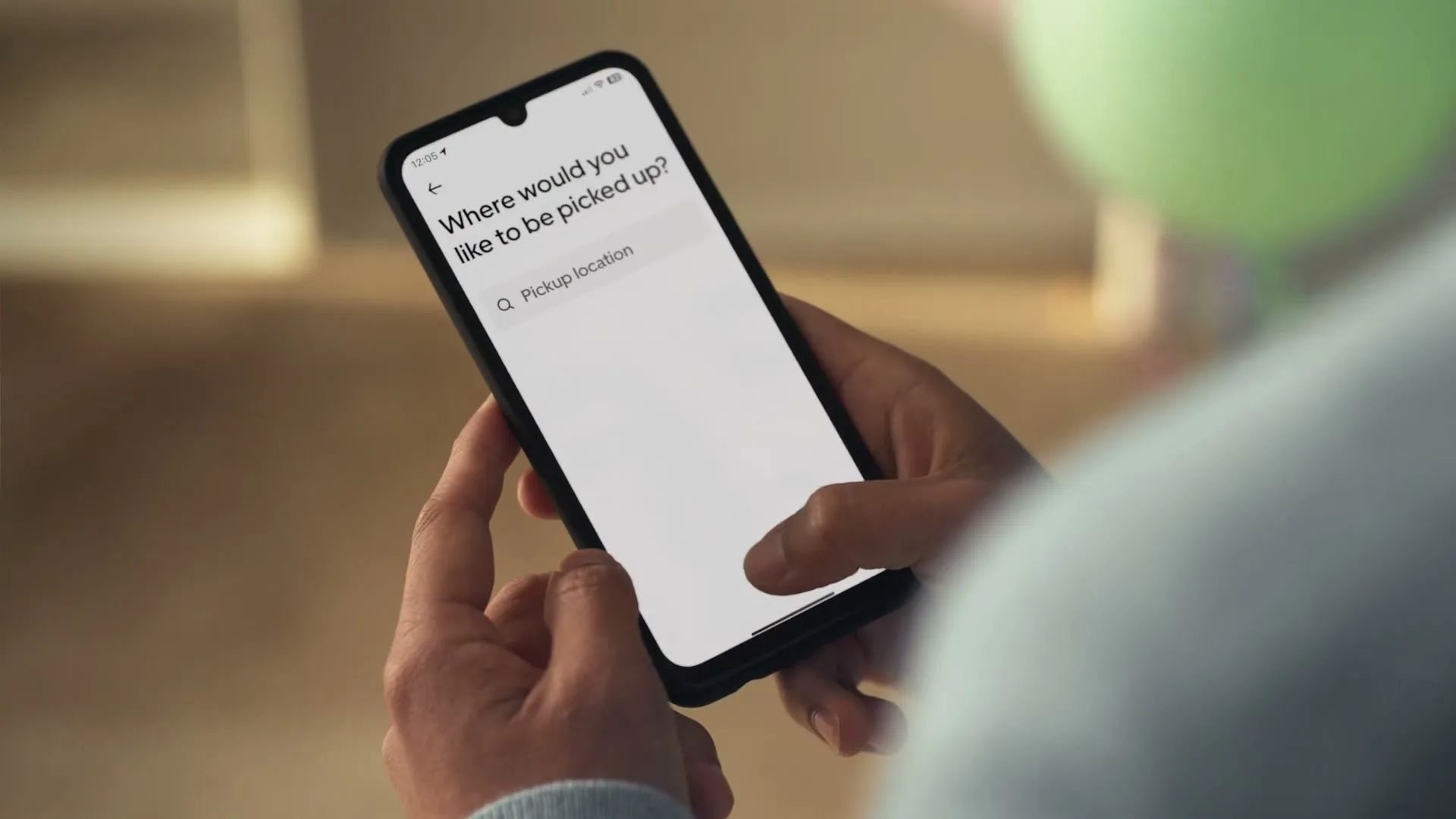A person's hands hold a smartphone, tapping on the screen to reserve an Uber ride, with a green balloon visible in the background.