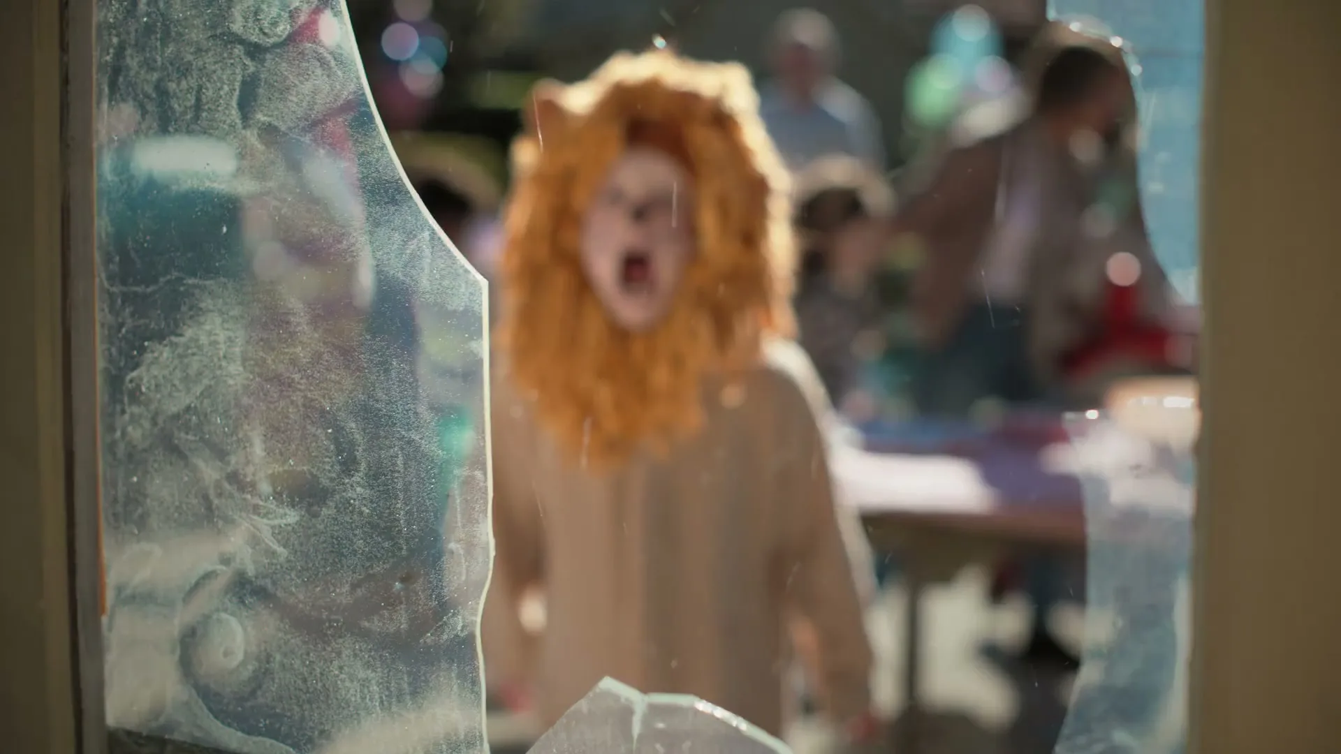 A soccer ball shatters a glass window, revealing a child in a lion costume screaming in a backyard party.