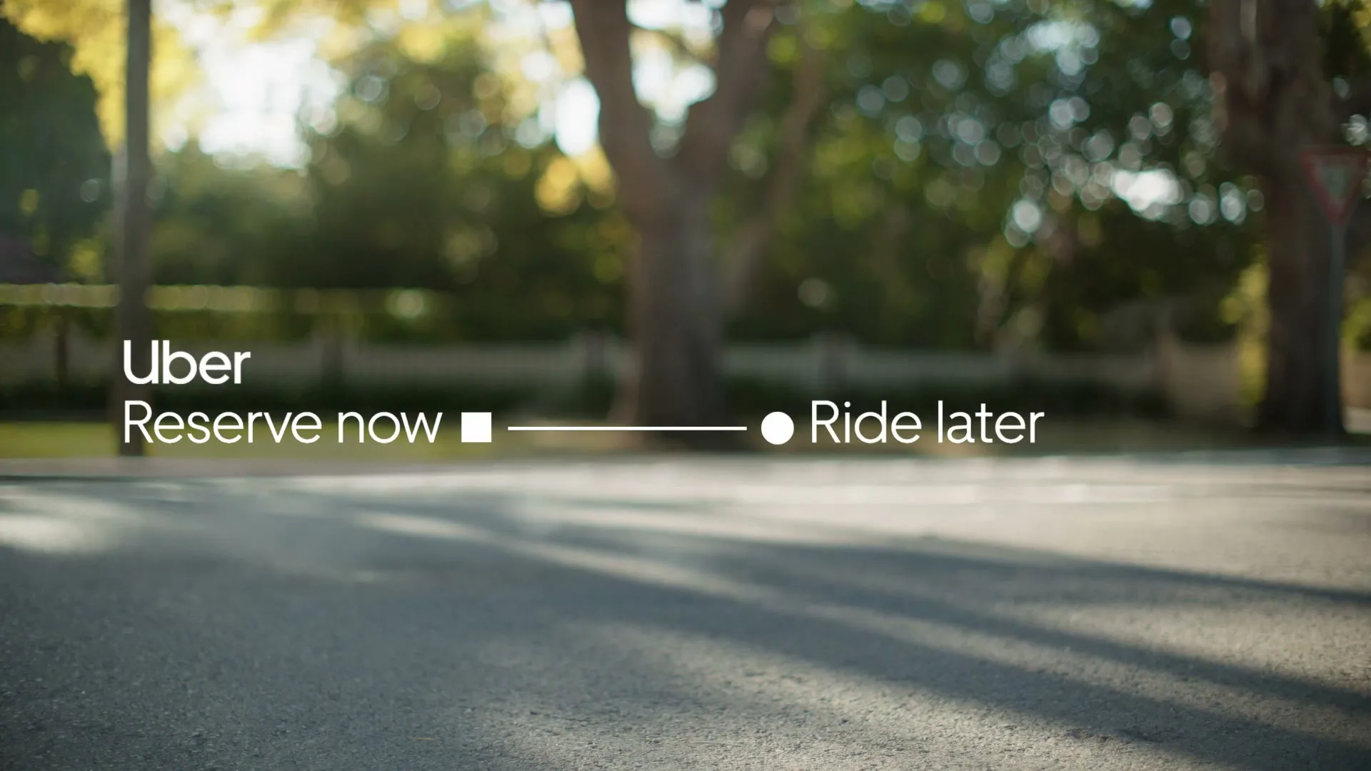 A dark blue car drives away on a sunny suburban street, with the Uber logo and text "Reserve now, Ride later" overlaid on the screen.
