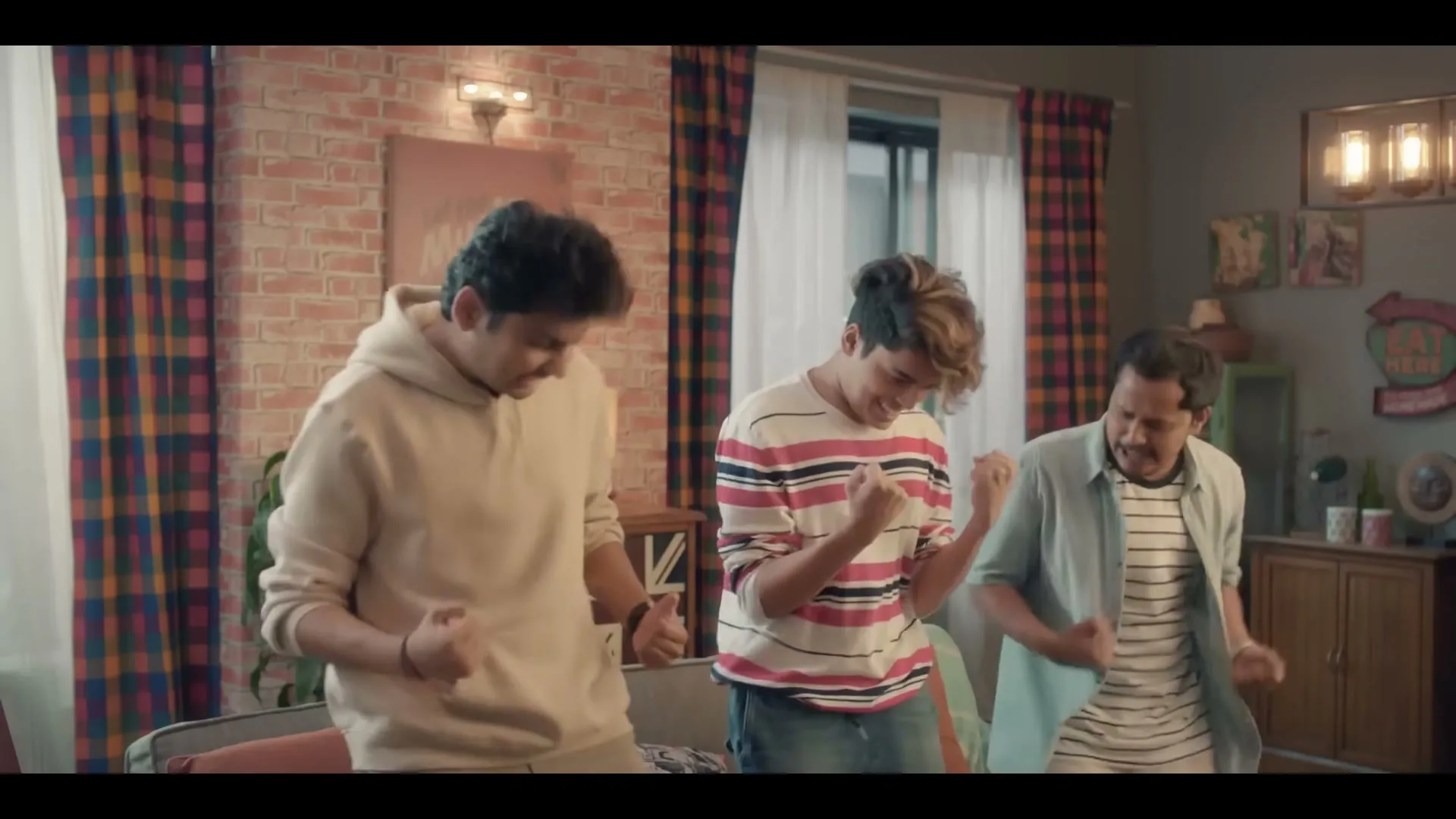 Three young men in casual clothes celebrate excitedly in a modern living room, jumping and cheering.