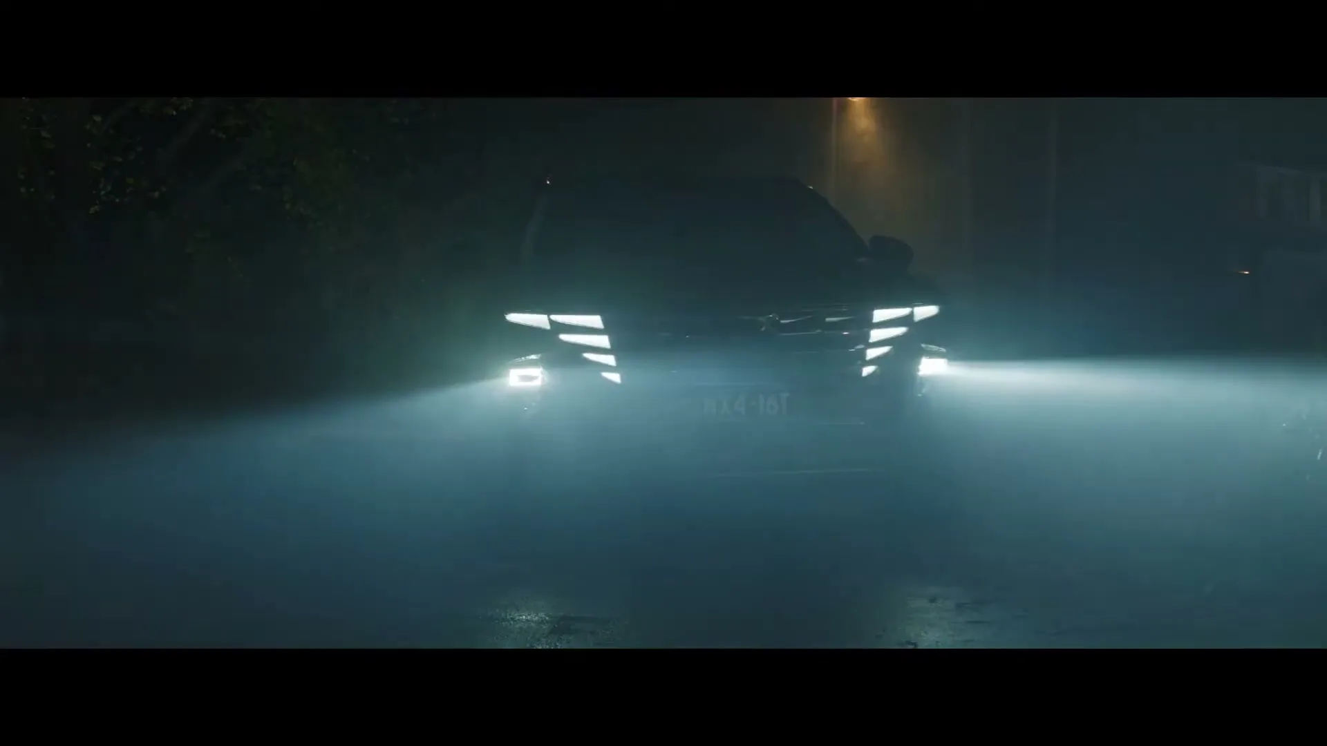 A dark SUV with bright, futuristic headlights drives towards the camera on a wet street at night, with a streetlamp glowing in the background.