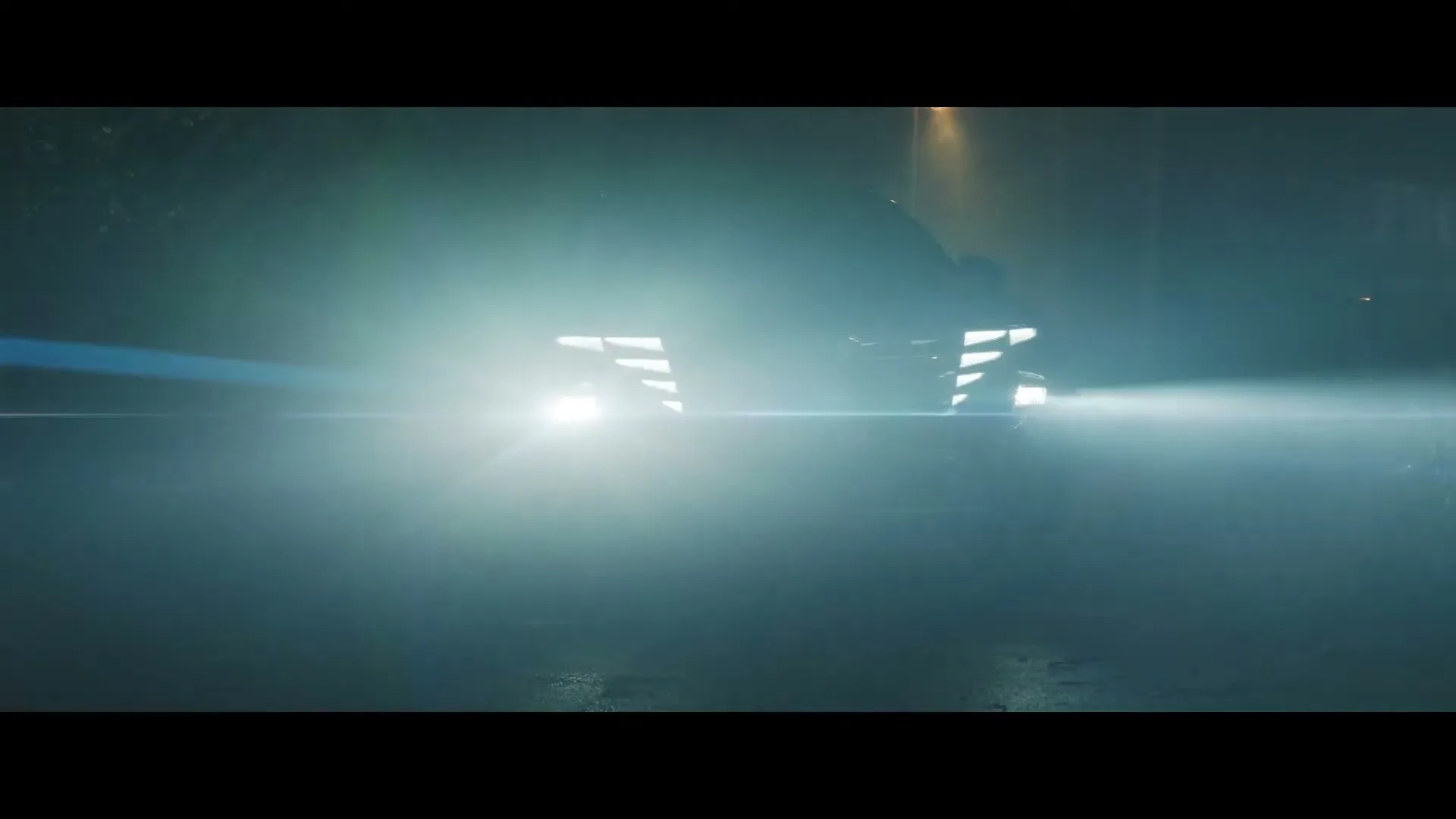 A dark car with bright headlights and distinctive daytime running lights drives towards the camera on a wet street at night.