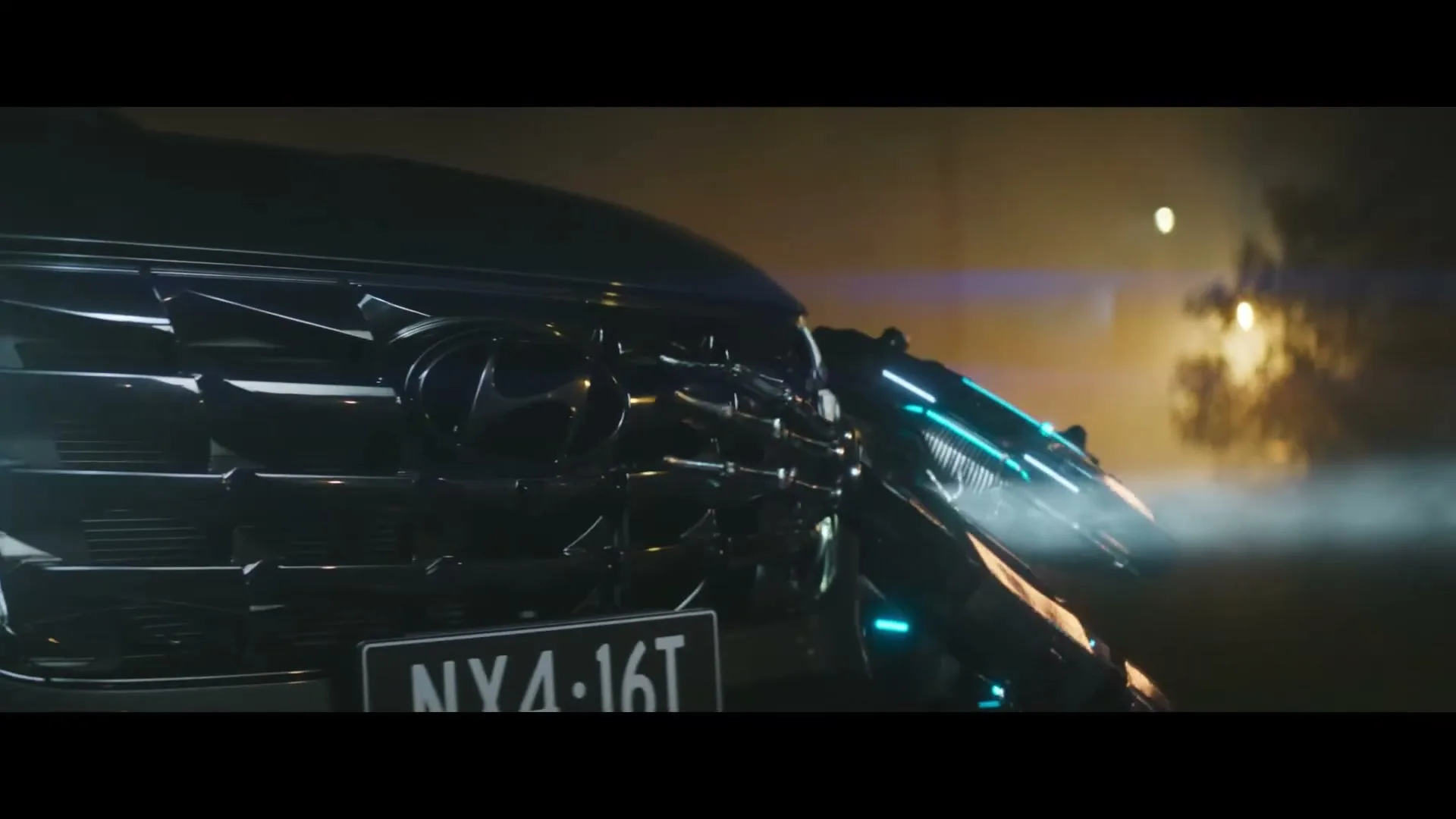A futuristic robot with glowing blue lights attempts to dismantle the front of a dark Hyundai car at night, with smoke and bright lights in the background.