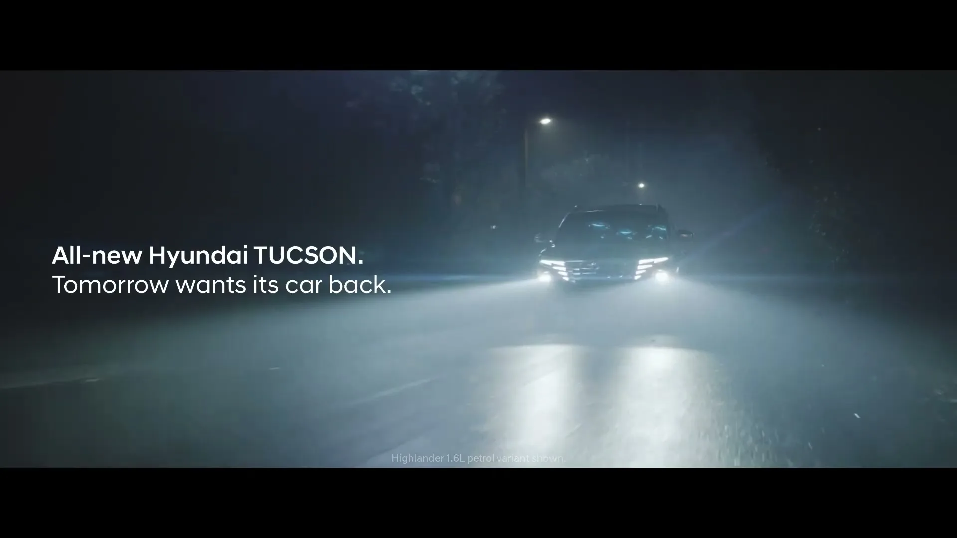 A Hyundai Tucson drives towards the camera on a dark, wet road at night, with its headlights brightly illuminating the misty path.