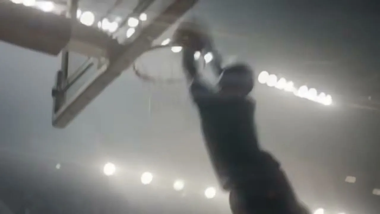 A male basketball player in silhouette dunks a basketball in a brightly lit arena.