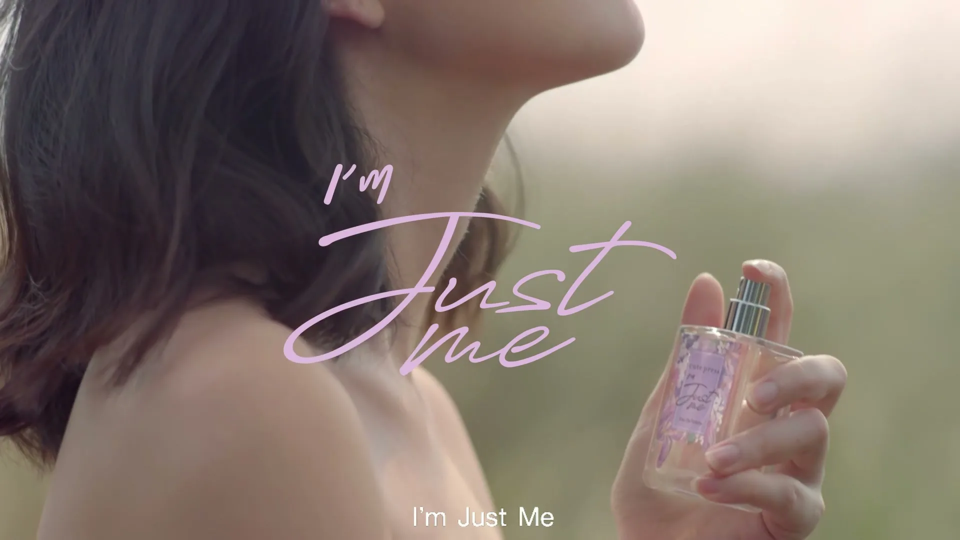A young woman with dark hair, wearing a strapless top, sprays perfume on her neck in an outdoor setting, with text overlay.
