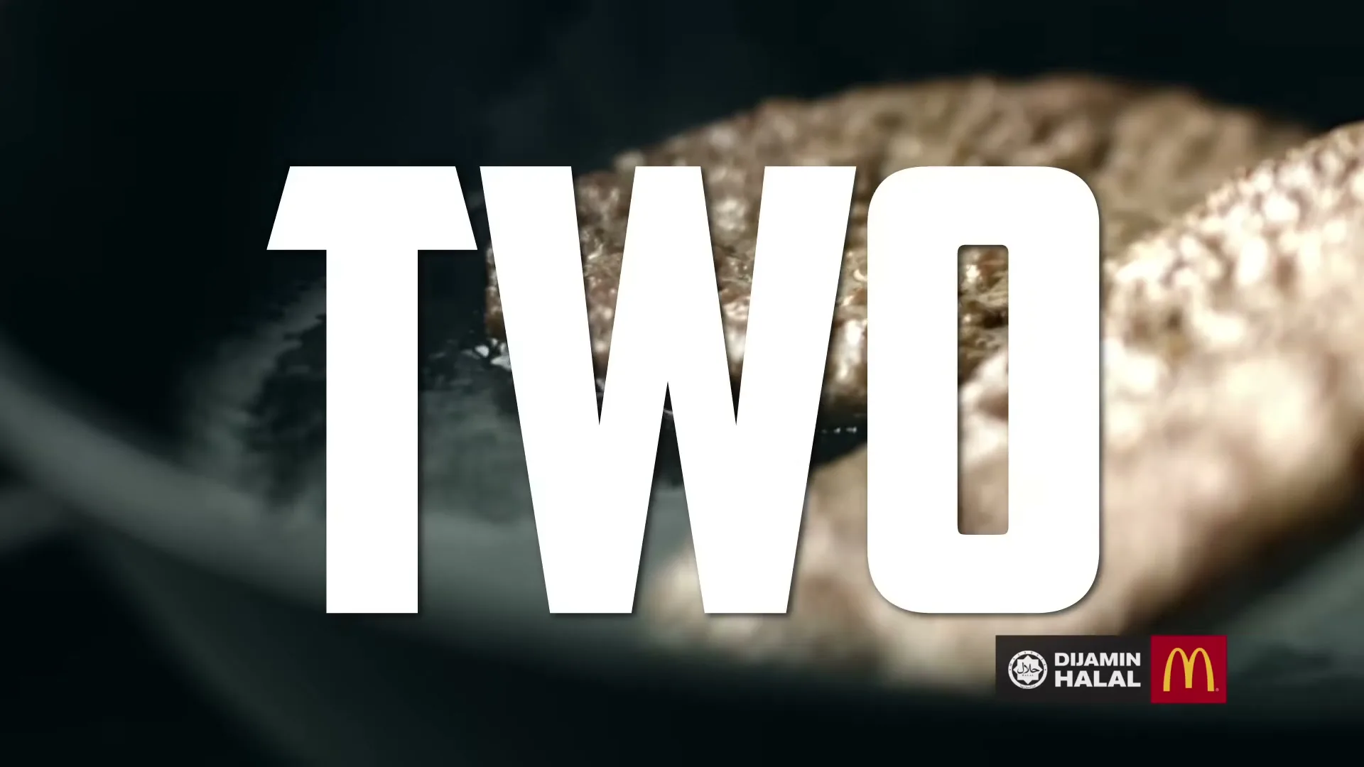 A close-up shot of two beef patties sizzling in a pan, with the word "TWO" in large white letters overlaid on the screen.