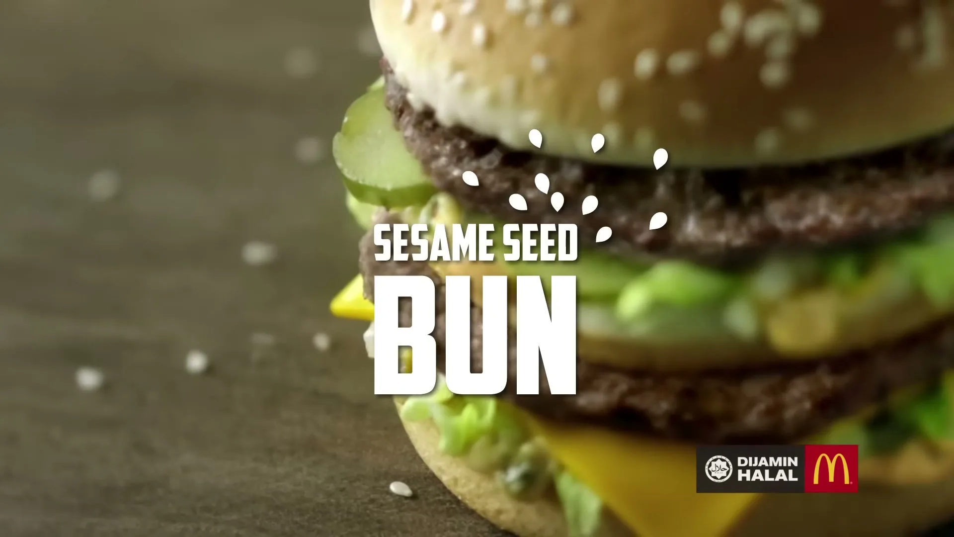 A close-up shot of a Big Mac burger with sesame seeds falling onto the top bun, with "SESAME SEED BUN" text on screen.