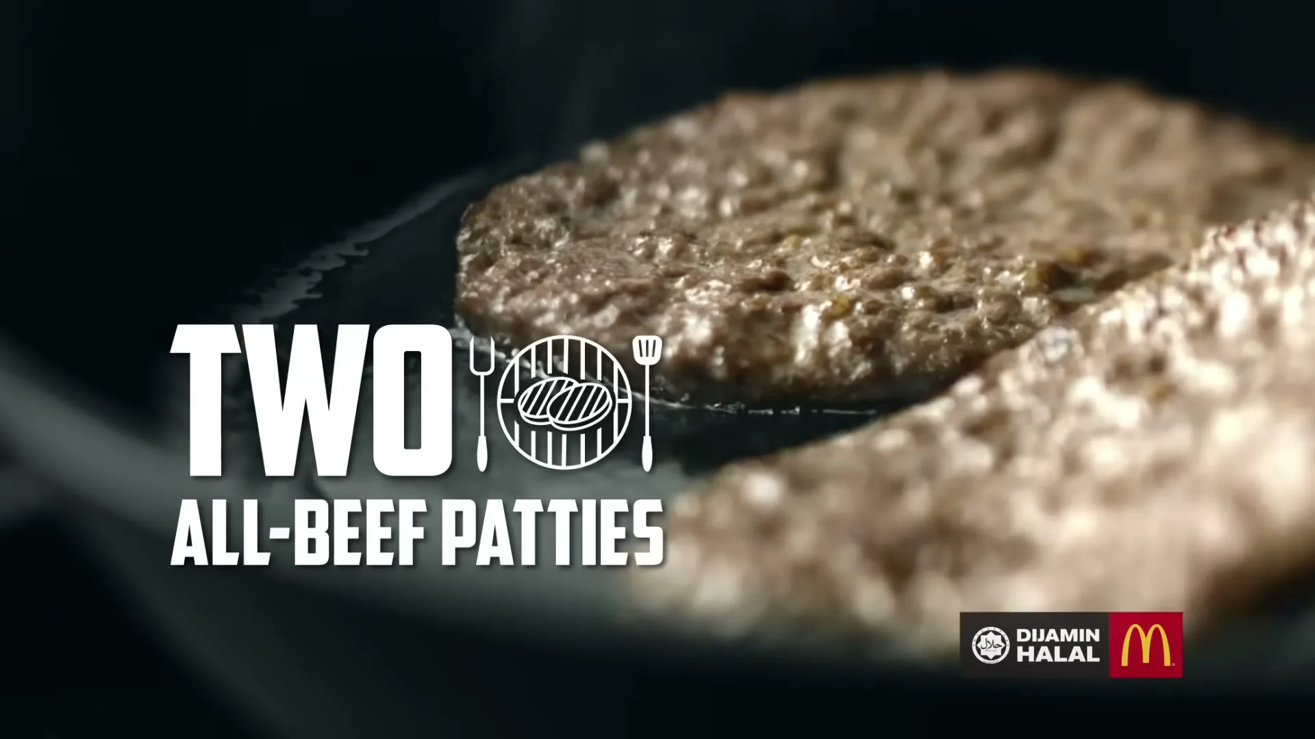 Two beef patties sizzle in a hot pan, with steam rising, as text appears on screen in a close-up shot.