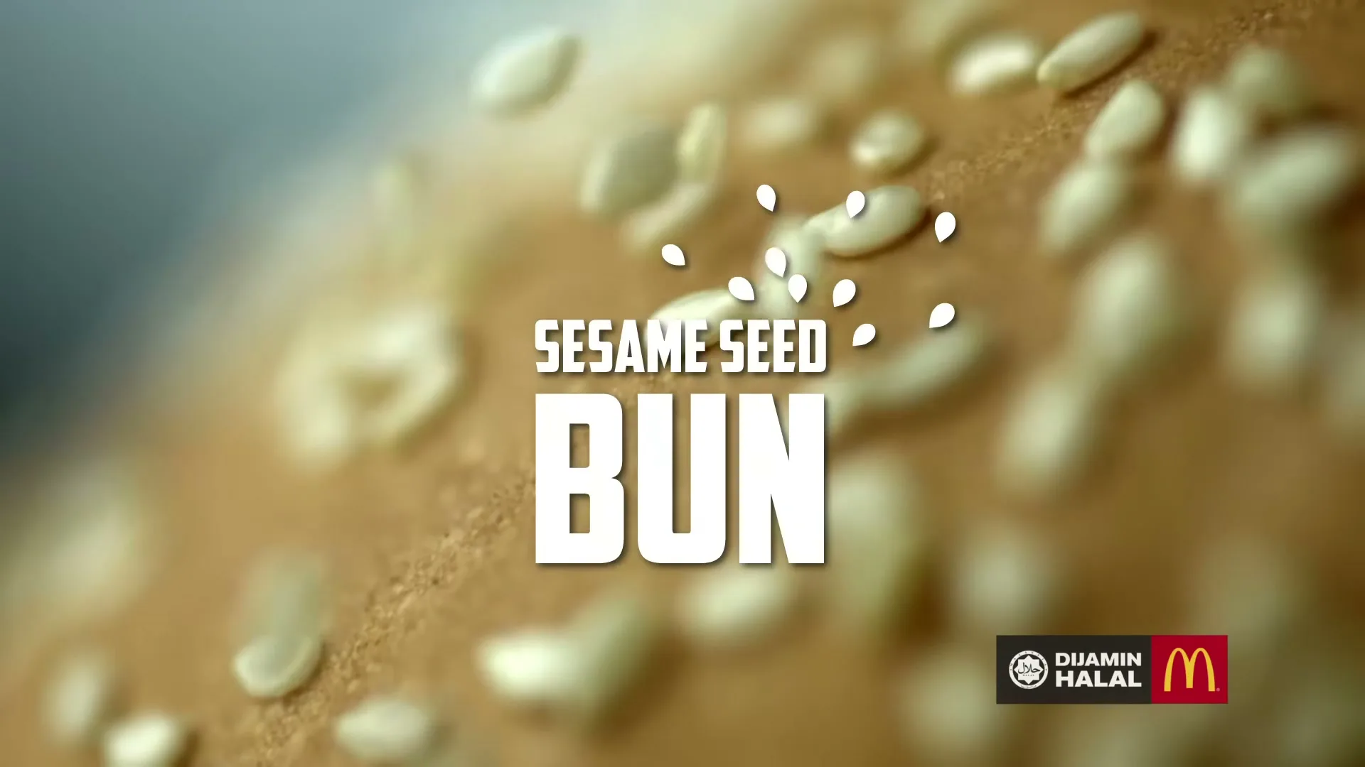 A close-up shot of a sesame seed bun with sesame seeds falling onto it, with text overlay and the McDonald's logo.