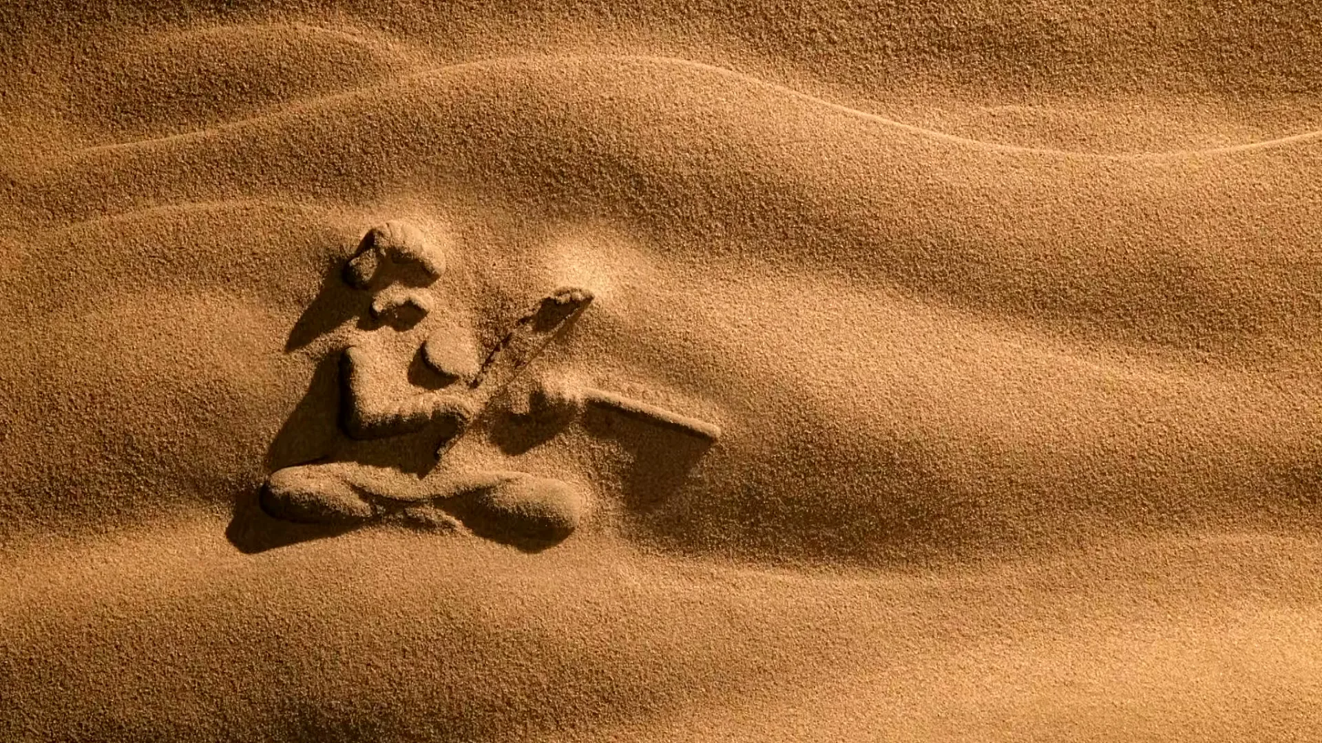 An animated sand carving of a person playing a stringed instrument is seen in a desert landscape, with sand blowing over it.