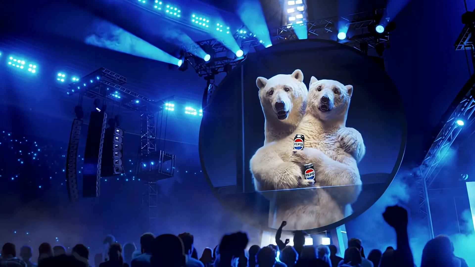 Two animated polar bears are shown on a large circular screen, holding Pepsi cans, as a crowd watches at a concert.