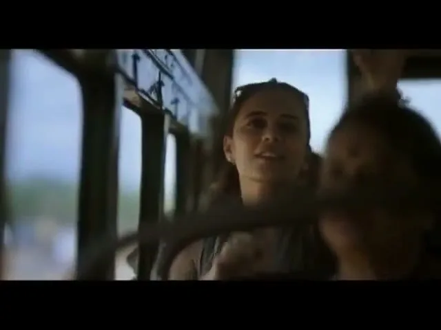 A young woman with sunglasses on her head looks out the window of a moving bus, with another person partially visible in the foreground.
