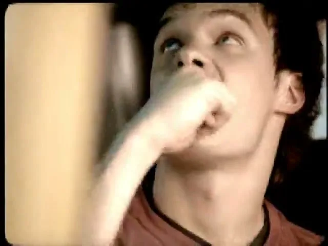 A young man with curly hair looks up, then takes a bite of a Snickers bar, in a close-up shot.