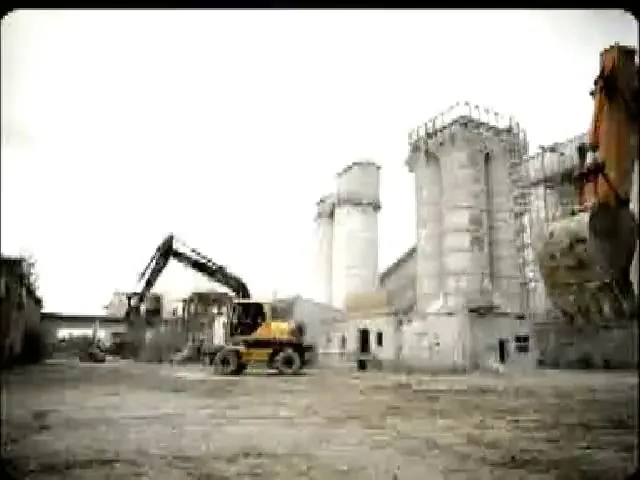 A wide shot of a desolate industrial area with an excavator and a Snickers bar flying through the air.