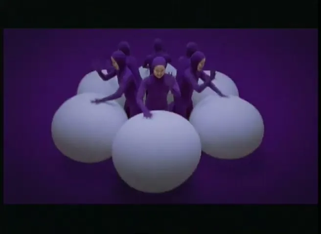 A group of people in purple bodysuits bounce on large white spheres against a purple background, creating a playful and surreal scene.