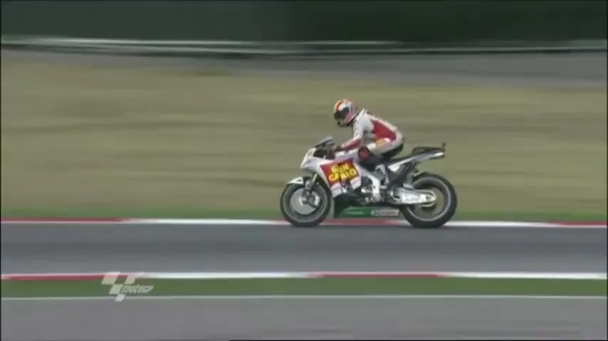 A motorcycle racer in a white and red suit speeds across a track during a race.