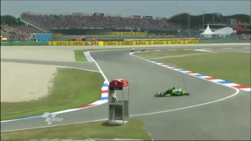 A green motorcycle racer crashes on a track, sliding across the asphalt while the camera zooms in on the action.